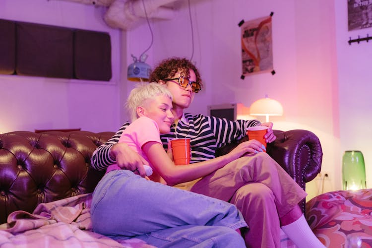 Sweet Couple Holding Plastic Cups While Sitting On The Couch 