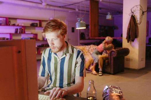 Man using computer while couple embraces on sofa in cozy room.