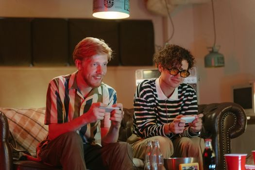 Two friends playing video games together on a cozy couch in a living room setting.