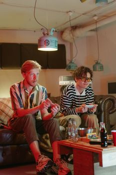 Two young men intensely playing video games on a cozy couch indoors.