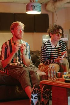 Teenagers engaged in a video game session on a couch in a warm-lit living room.