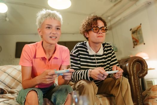 A young couple sitting on a sofa, intensely focused while playing video games indoors.