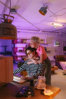 A young couple shares a tender embrace while using a vintage computer in a retro-styled room.