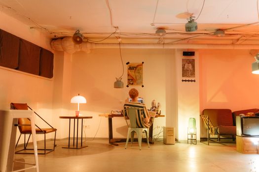 A man sits at his laptop working late at night in a warmly lit, cozy room.