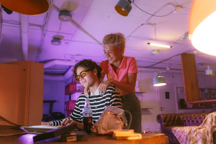 Smiling Woman Standing Over Man Sitting By Computer