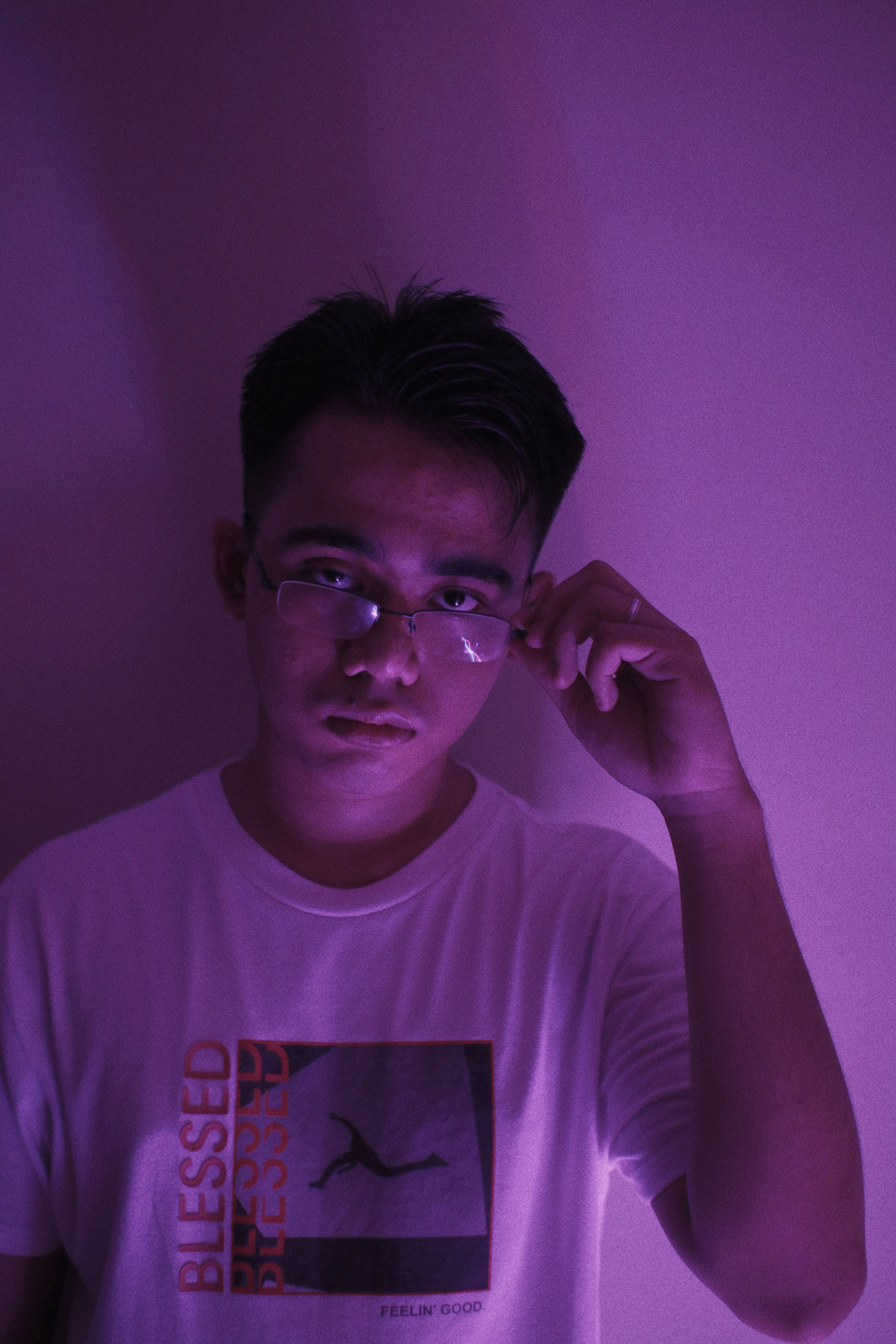Portrait of a young man adjusting his sunglasses under dramatic purple lighting.