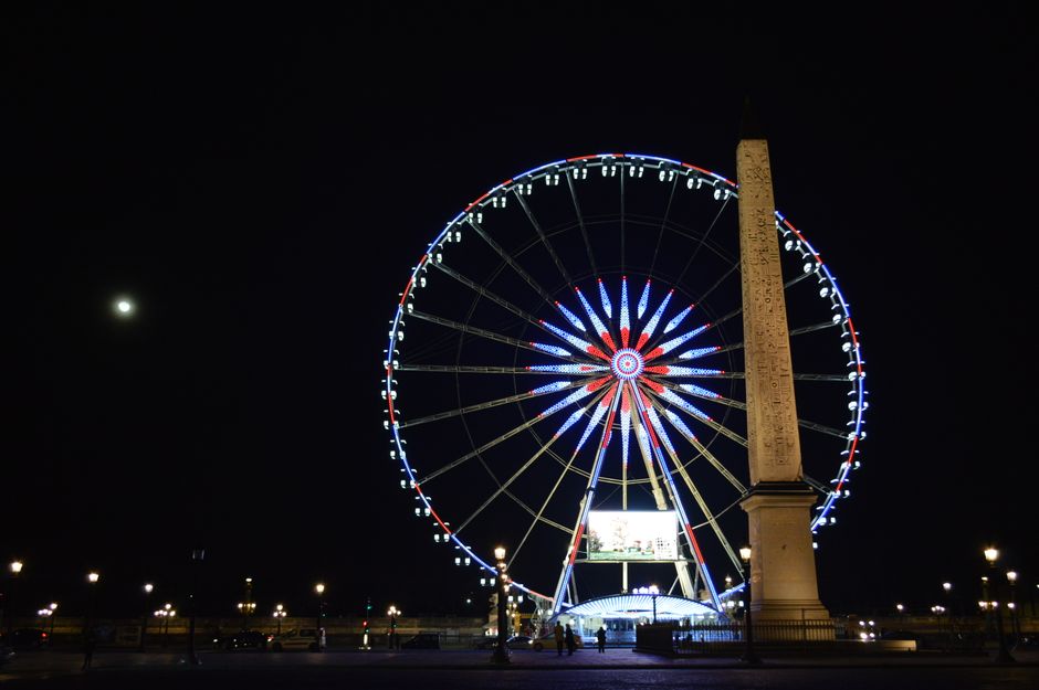 A stunning view of a lit Ferris wheel beside the ancient Obelisk in Paris, France at night.