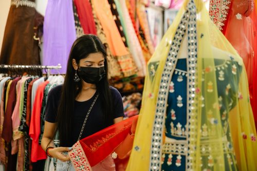 Free A woman wearing a face mask shops for traditional attire in a vibrant boutique. Stock Photo
