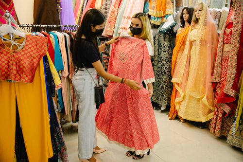 Free Two women browsing traditional dresses in a colorful boutique setting. Stock Photo