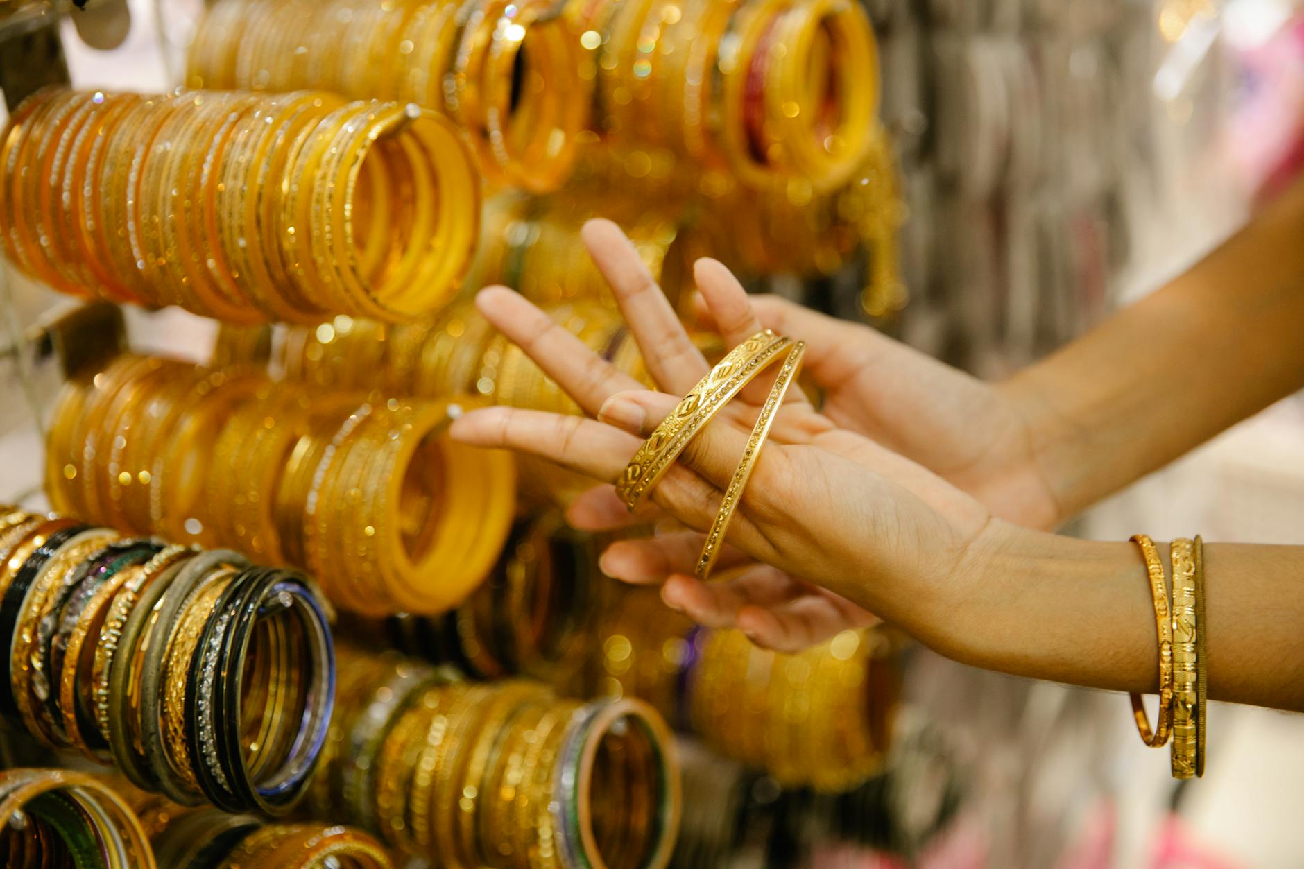 A close-up of a woman's hands selecting golden bangles at a jewelry store, showcasing intricate designs.