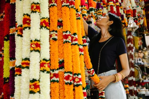 Free A woman in a market surrounded by vibrant, handmade flower garlands exploring traditional crafts. Stock Photo