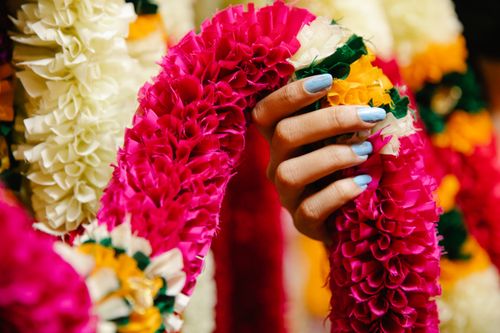 Free A vibrant hand with painted nails holding a colorful flower garland, captured in close-up. Stock Photo