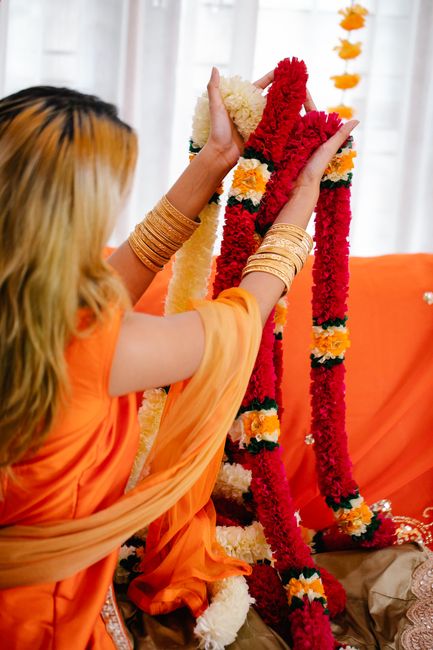 Back view of a woman in orange holding vibrant floral garlands in a festive setting.