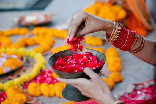 Close-up of hands holding a bowl of red petals during a colorful Indian flower ceremony.