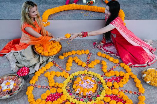 Two women in traditional attire creating vibrant floral decorations for an Indian festival celebration.