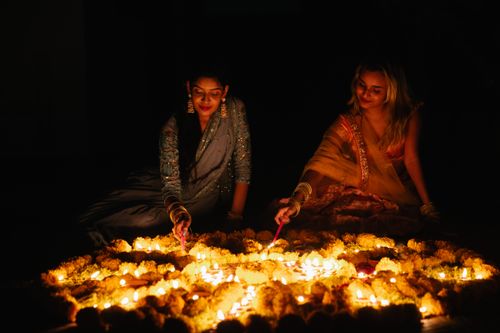 Free Two women light candles surrounded by flowers during a traditional night festival celebration. Stock Photo