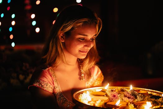 A woman in traditional attire holds a tray of lit candles during a vibrant cultural celebration.