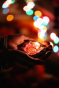 Close-up of hands holding a decorative Diwali candle with colorful bokeh lights in the background, creating a festive atmosphere.