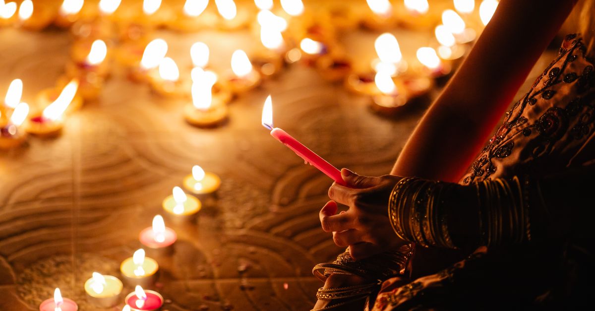 A close-up of hands holding a candle during a Diwali festival, surrounded by glowing candles.