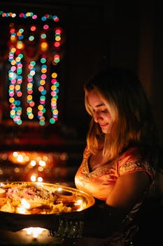 A woman in traditional dress holds a tray with lit candles, surrounded by colorful lights.
