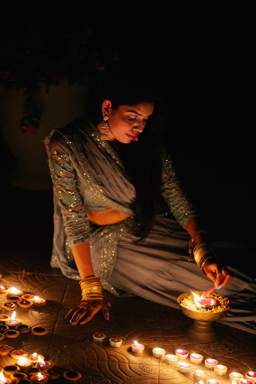 A Woman in Elegant Dress Sitting on the Floor Lighting a Candle