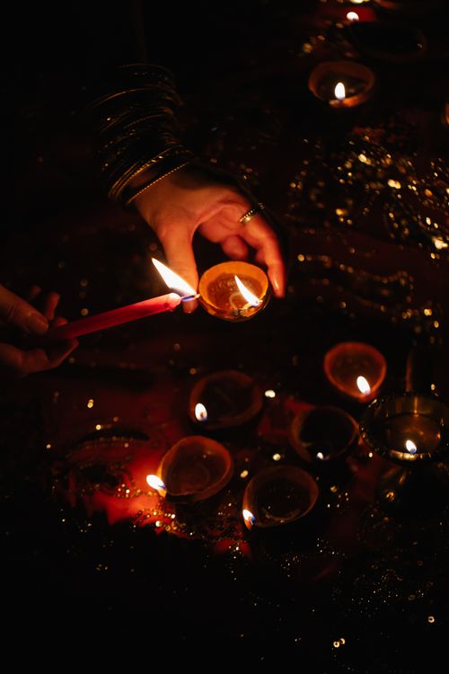 Free A hand lighting diyas with a candle, capturing the festive Diwali atmosphere. Stock Photo