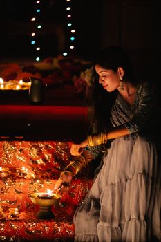 South Asian woman lights a diya in a traditional ceremony, surrounded by candles.