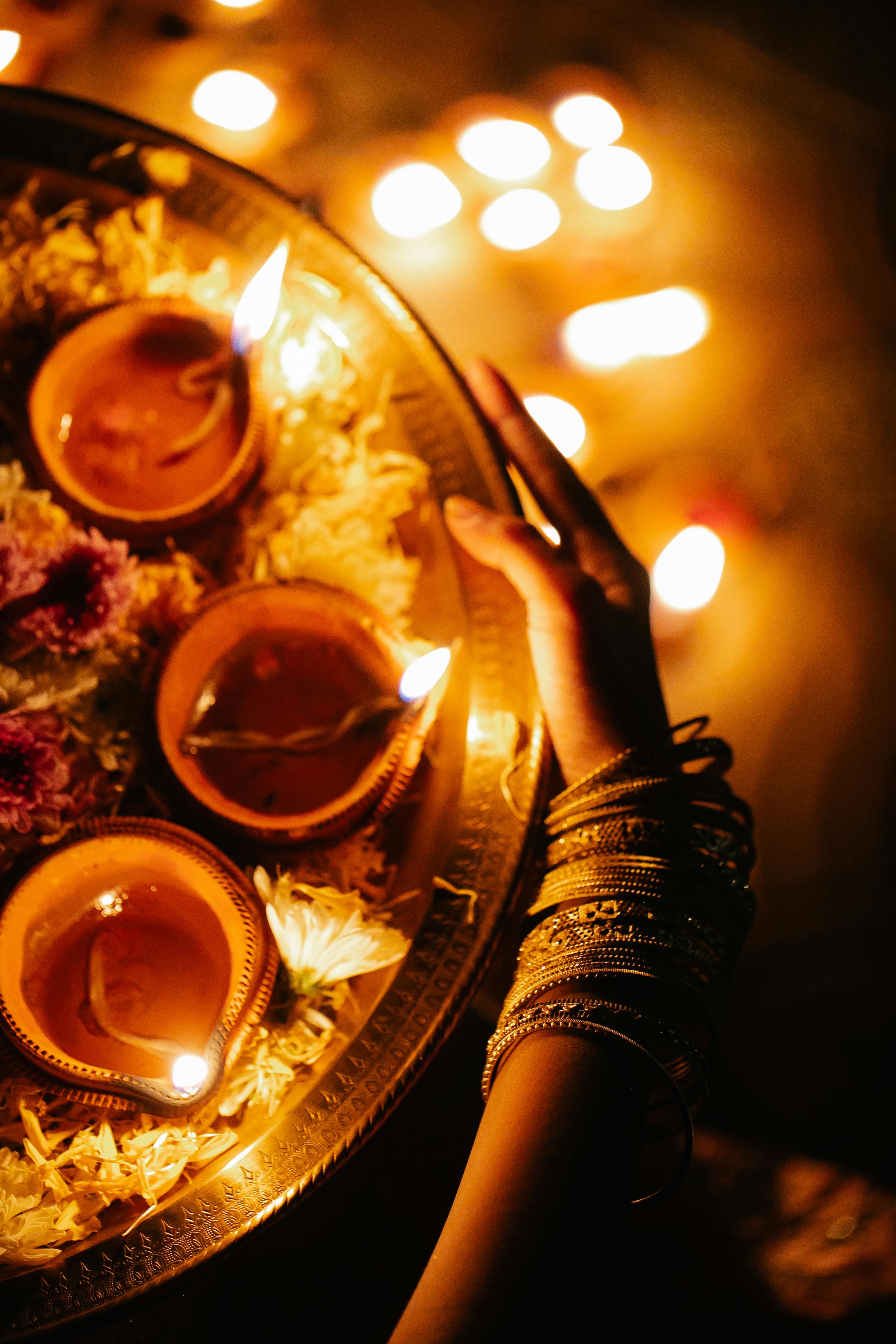 a person wearing bracelets holding a tray with flowers and candlelight