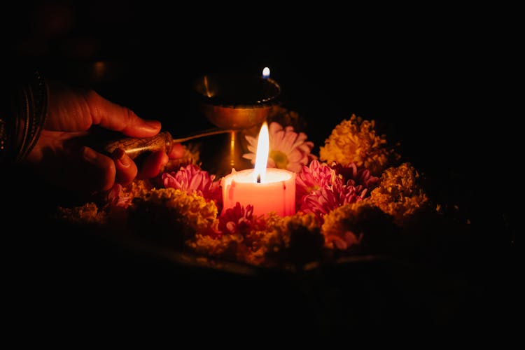 A Person Holding A Stick On A Lighted Candle With Flowers