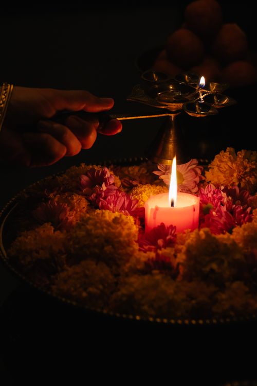 Free A close-up of a traditional Indian candlelight ceremony with flower arrangements and a hand lighting candles. Stock Photo