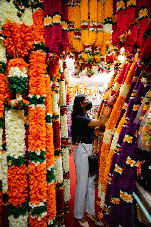 Free A woman wearing a mask shops for colorful flower garlands indoors. Stock Photo