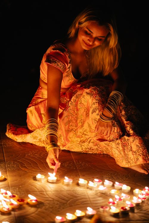 Free A woman dressed in traditional attire illuminates diya candles, creating a festive ambiance. Stock Photo