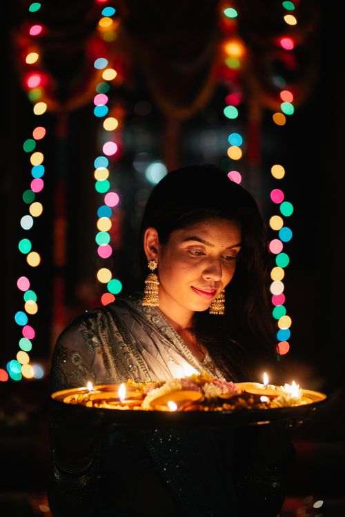 Free A woman in traditional attire holding a plate of lit diyas during a festive celebration. Stock Photo