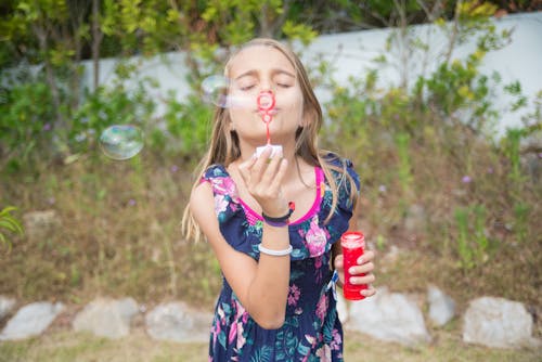 Free Young Girl in Floral Dress Blowing Bubbles Stock Photo