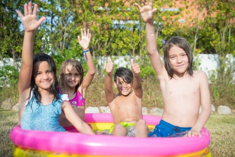 Kids Wearing Swimwear Sitting On Pink And Yellow Inflatable Swimming Pool