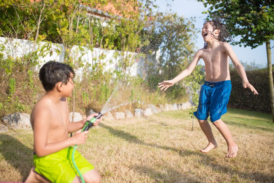 Two children enjoying a playful moment with a garden hose on a sunny day.