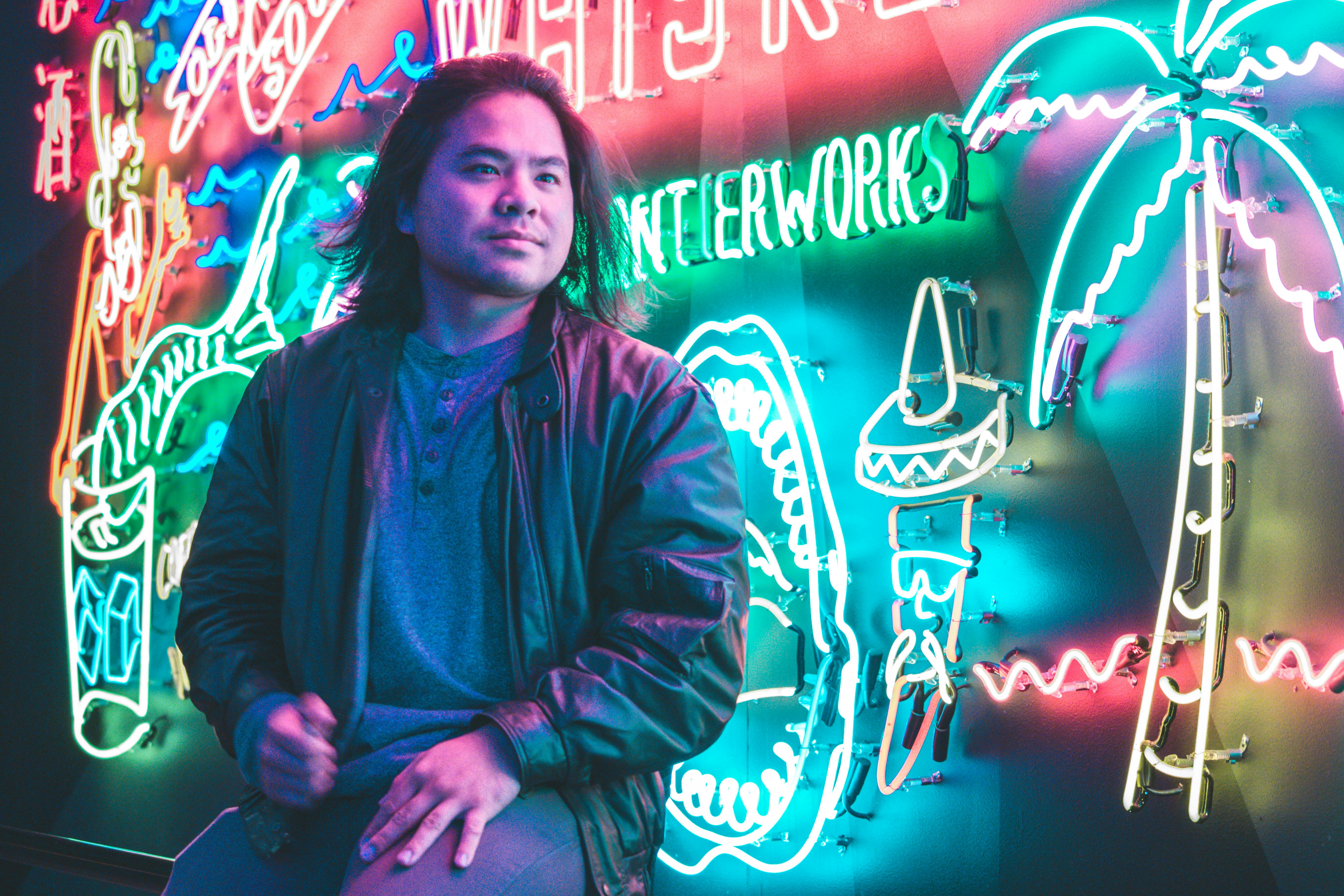 Man posing in front of colorful neon signs in a nightclub setting, embodying vibrant nightlife.