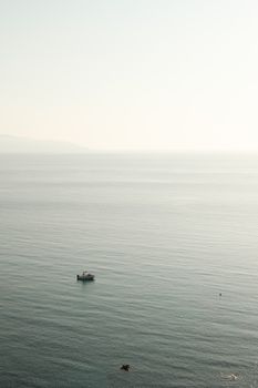 A serene aerial shot of a lone boat navigating calm open water under clear sky, perfect for tranquil themes.