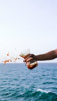 A hand pours a vibrant golden liquid over ocean waves, capturing motion and tranquility.