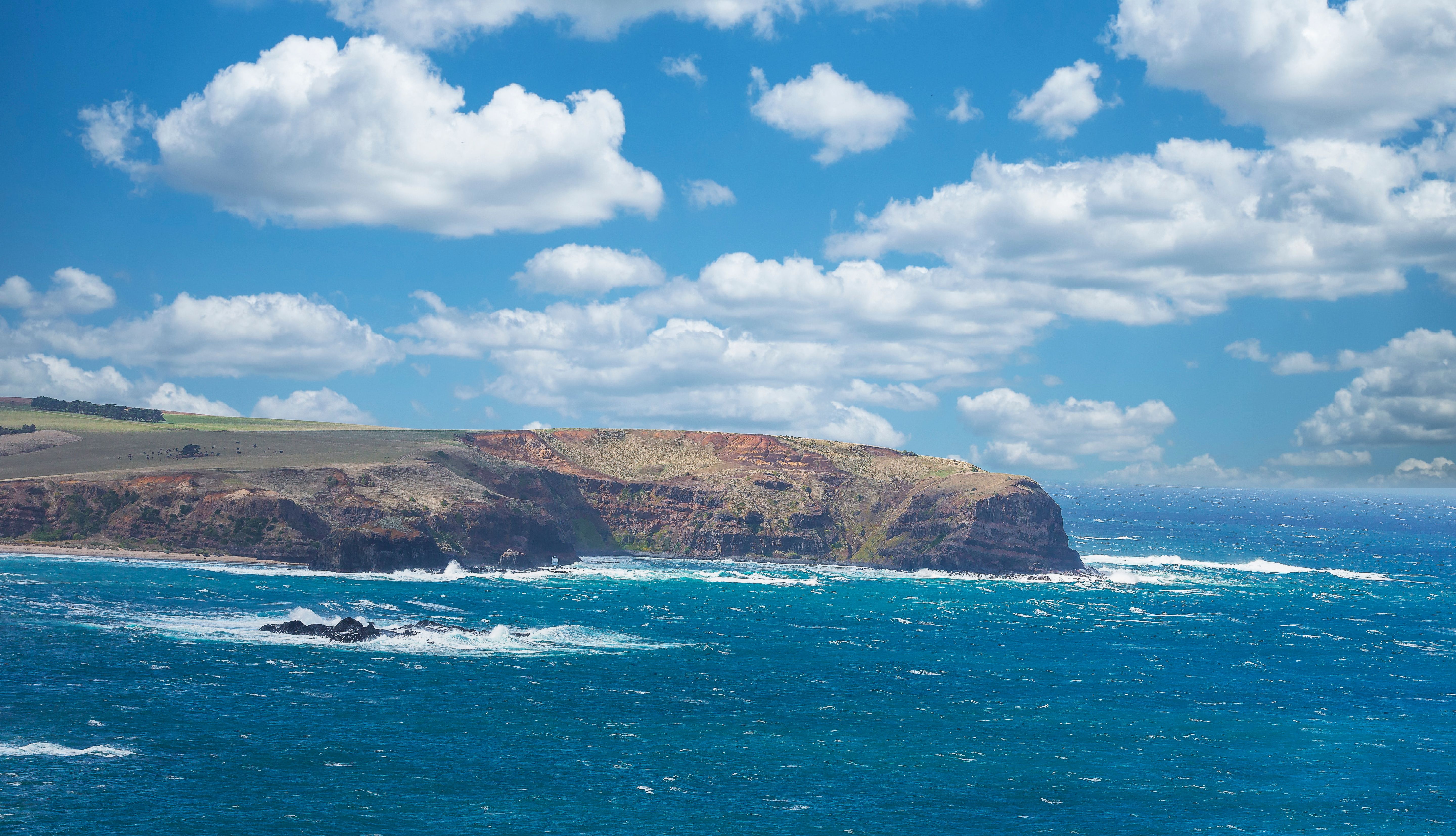 Vivid seascape of rocky cliffs and blue ocean under a partly cloudy sky.