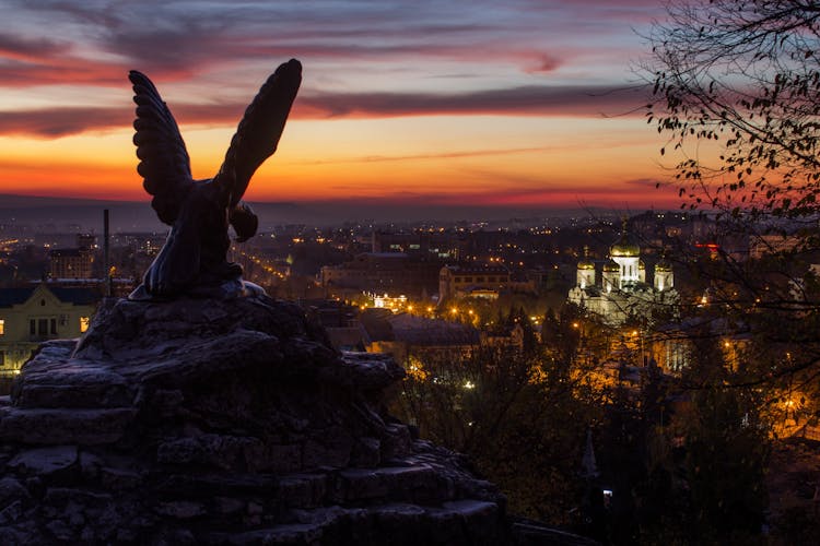 Sculpture On Hill Overseeing Night City In Lights