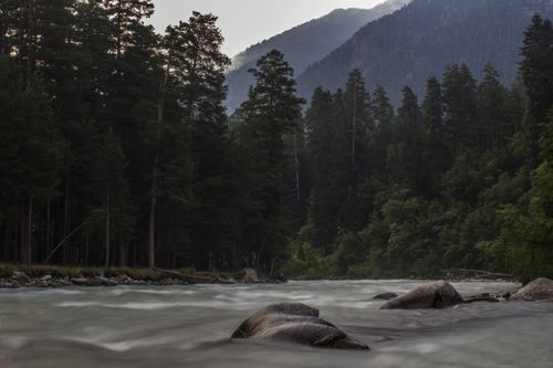 Free A serene river meandering through lush forest and majestic mountains at daytime. Stock Photo