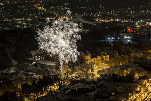 A breathtaking aerial shot of a winter cityscape illuminated by fireworks at night, celebrating festivity.