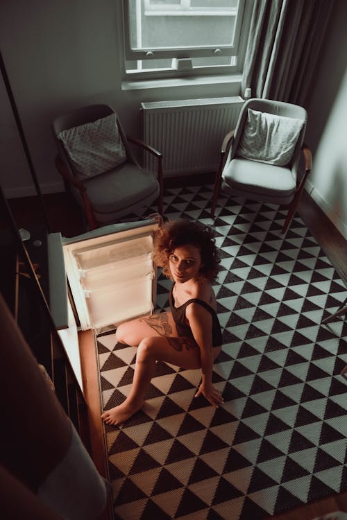 High Angle Shot of Woman Sitting In Front of a Refrigerator 