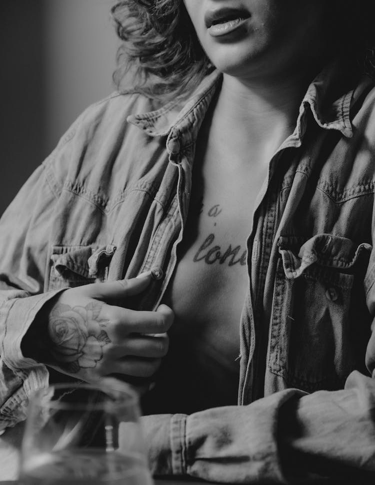 A Woman In Button Up Shirt Showing A Chest Tattoo