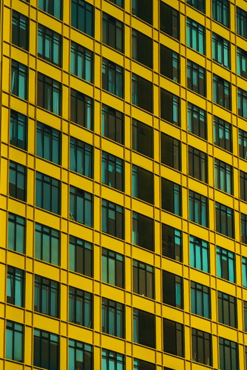 Free Close-up of a modern yellow building facade with reflective glass windows in a vertical pattern. Stock Photo