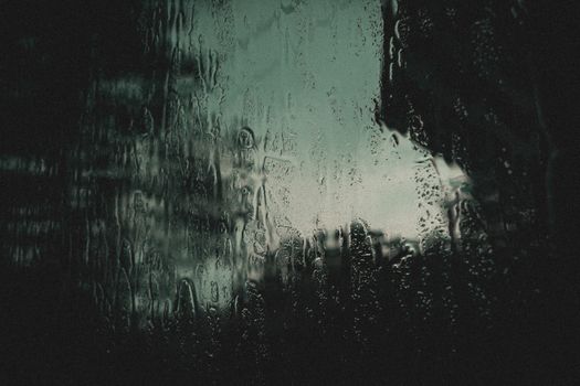Artistic capture of raindrops on glass with a dark and moody atmosphere. Ideal for backgrounds.