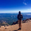 一名独自徒步旅行者背着背包，站在科罗拉多州的派克峰顶上，欣赏着令人惊叹的山景