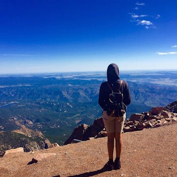 一名独自徒步旅行者背着背包，站在科罗拉多州的派克峰顶上，欣赏着令人惊叹的山景