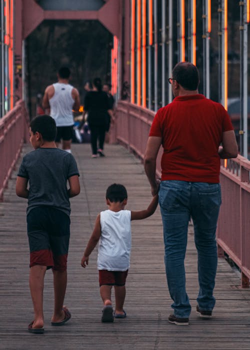 Free Father and two sons walking on a colorful footbridge at dusk, bonding and family time. Stock Photo